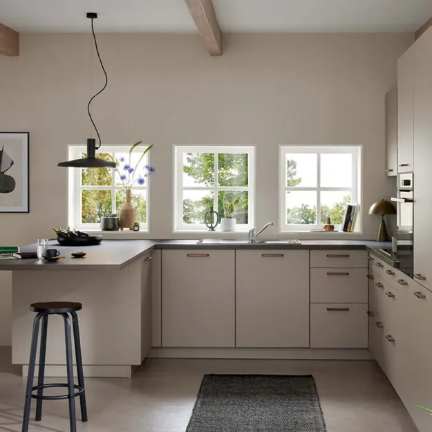 Helle Burger Küche in warmen Beigetönen mit L-förmiger Küchenzeile, Thekenbereich mit Hocker und großen Fenstern für viel Tageslicht